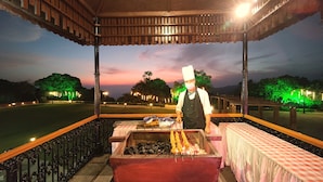 A chef preparing food at an outdoor grill with a view of a park and trees in the background. - Regenta MPG Club (Mahabaleshwar)