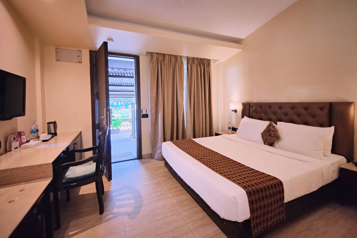 A hotel room with a bed, a desk with a chair, a television, and a door leading to an outdoor area.