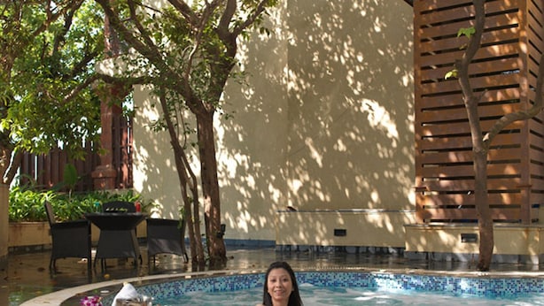 A woman relaxing by a pool with a drink, surrounded by trees and a tiled wall. - Regenta MPG Club (Mahabaleshwar)