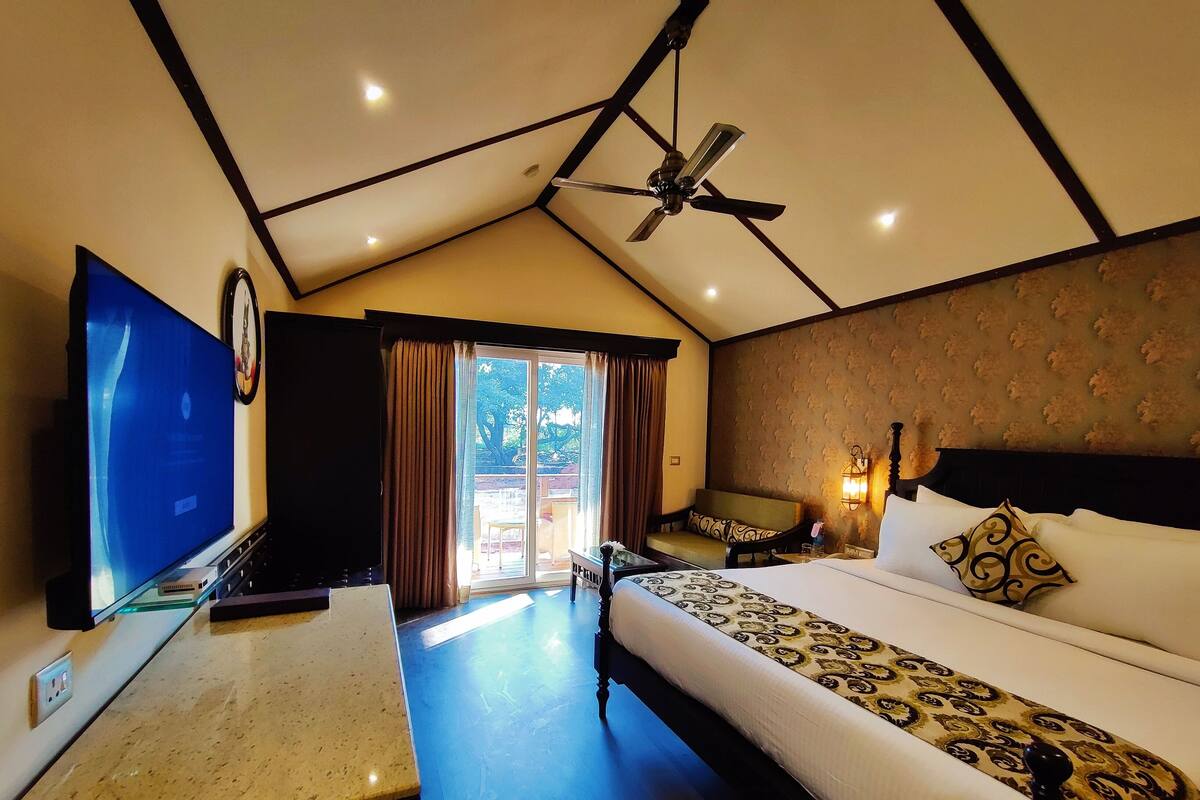 A hotel room with a bed, a desk with a flat-screen TV, a ceiling fan, and a view of the outdoors through a sliding door.