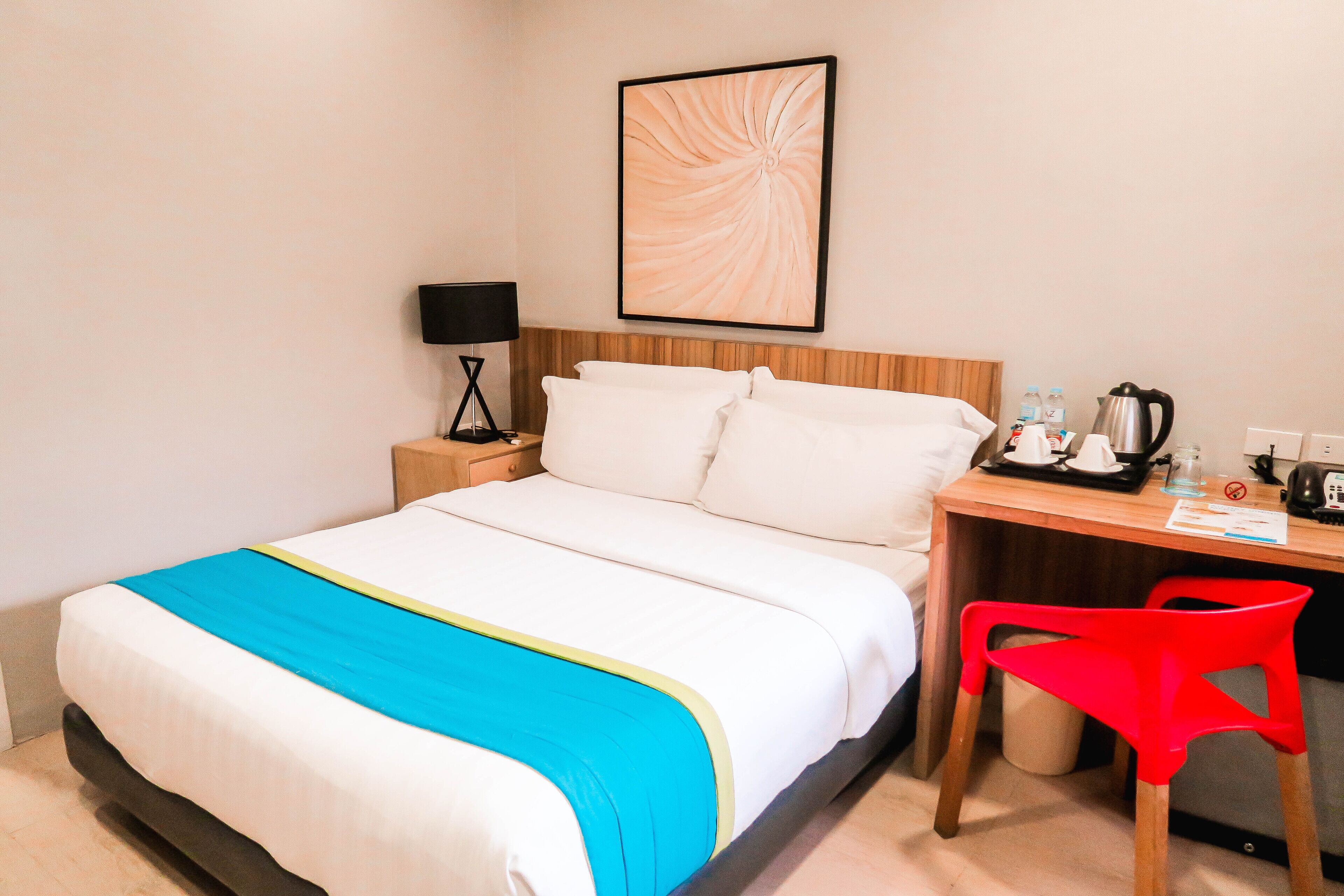 A hotel room with a bed, a desk, a chair, a lamp, and a framed picture on the wall.