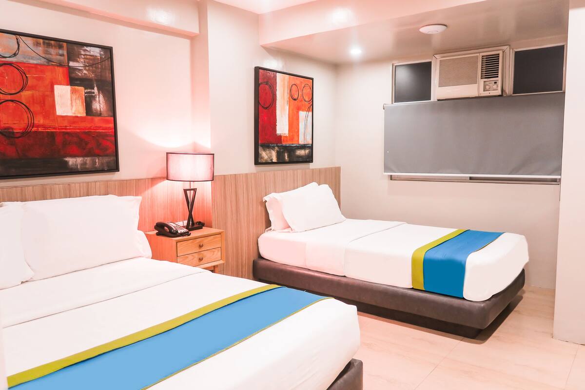 A hotel room with two beds, a bedside table with a lamp, and artwork on the walls.