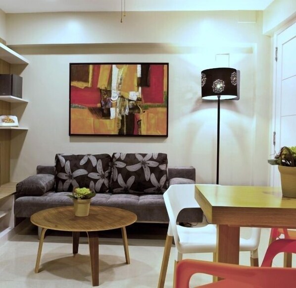 Una sala de estar moderna con un sofá gris, una mesa de centro redonda de madera, una silla blanca y una lámpara de pie.