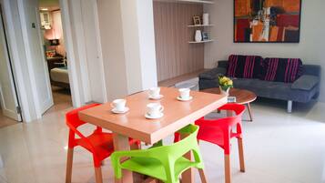 A modern living room with a wooden dining table, red and green chairs, a grey sofa, and a painting on the wall.
