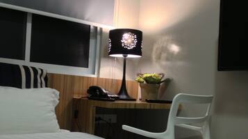 A hotel room with a bed, a desk with a chair, a lamp, and a wall-mounted TV.