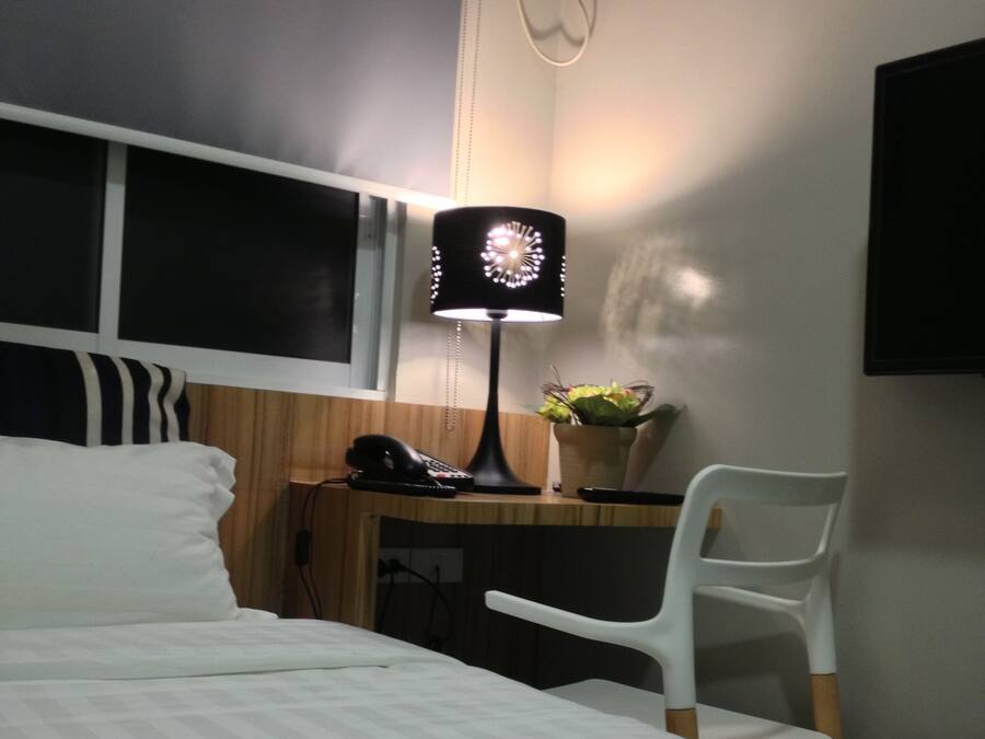 A hotel room with a bed, a desk with a chair, a lamp, and a wall-mounted TV.