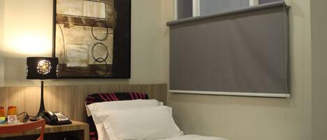 A hotel room with a bed, a desk with a lamp, a phone, and a window with a blind.