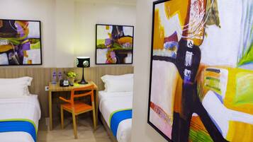 Une chambre d’hôtel avec deux lits, un bureau et une chaise. Trois œuvres d’art encadrées sont accrochées au mur.
