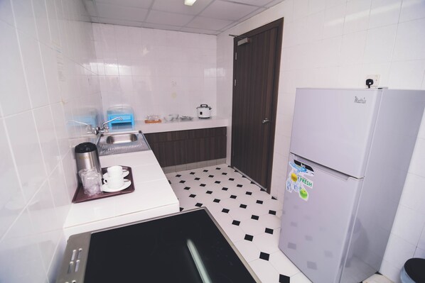 Una cocina compacta con baldosas blancas y negras a cuadros, un lavamanos de acero inoxidable, una encimera blanca, un refrigerador y un microondas.