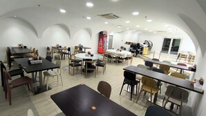 A conference room with multiple tables and chairs, a red Coca-Cola refrigerator, and a kitchen area in the background. - Jubilee Hotel (Bandar Seri Begawan)