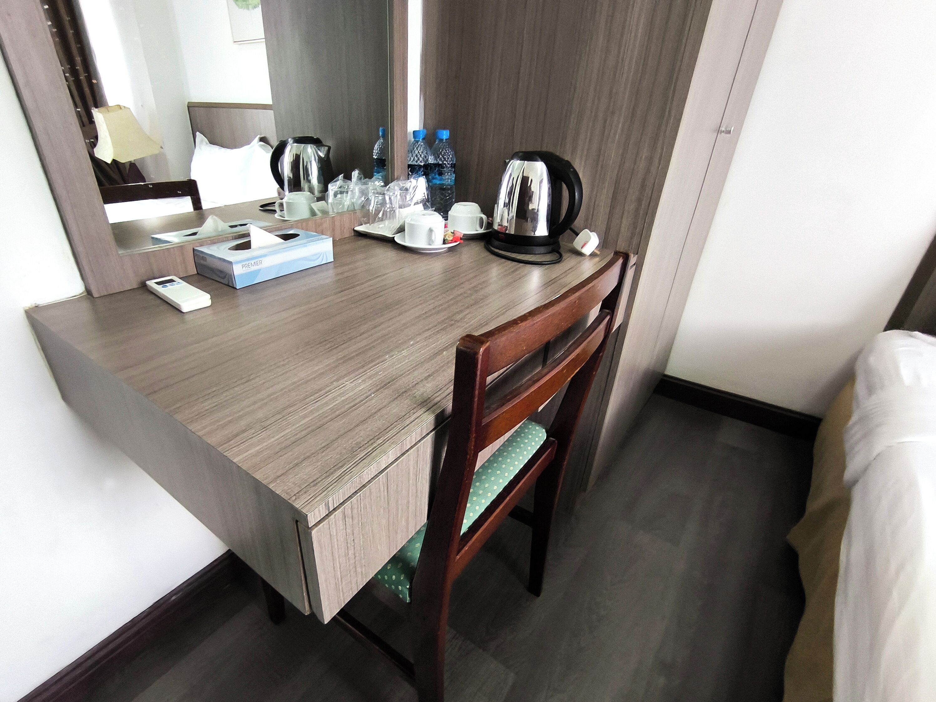 Une chambre d’hôtel équipée d’un bureau en bois, d’une chaise, d’un lit, d’un miroir, d’une machine à café et d’articles de toilette.