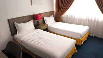 A hotel room with two beds, a desk, a chair, a nightstand with a lamp, and a window with curtains.