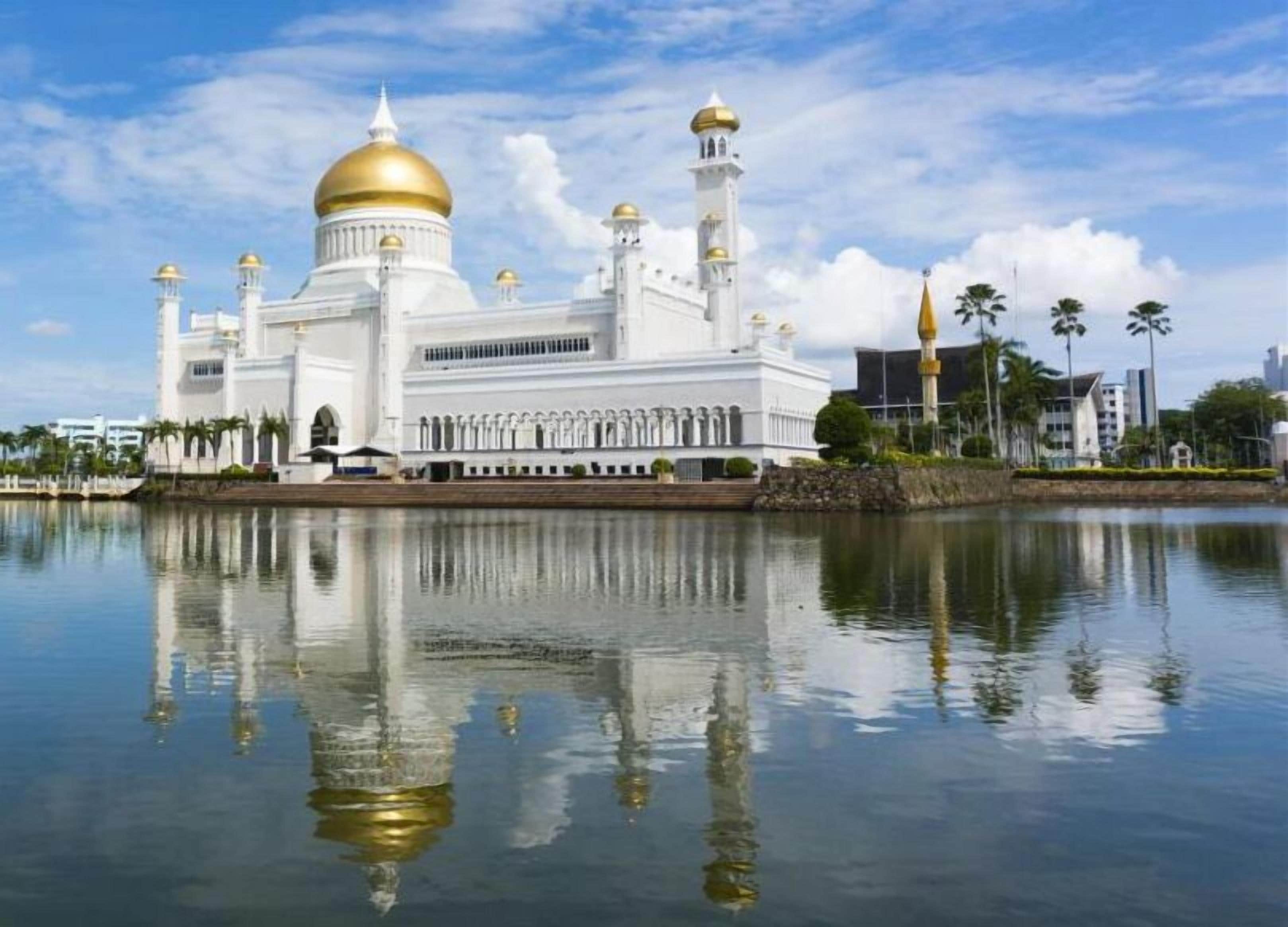Une grande mosquée blanche, avec des dômes et des minarets dorés, qui se reflète dans l’eau calme.