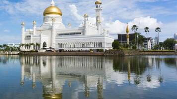 Una gran mezquita blanca con cúpulas doradas y minaretes, reflejada en aguas tranquilas.