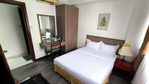 A hotel room with a bed, bedside table, desk, chair, mirror, and a wall-mounted air conditioner. - Jubilee Hotel (Bandar Seri Begawan)
