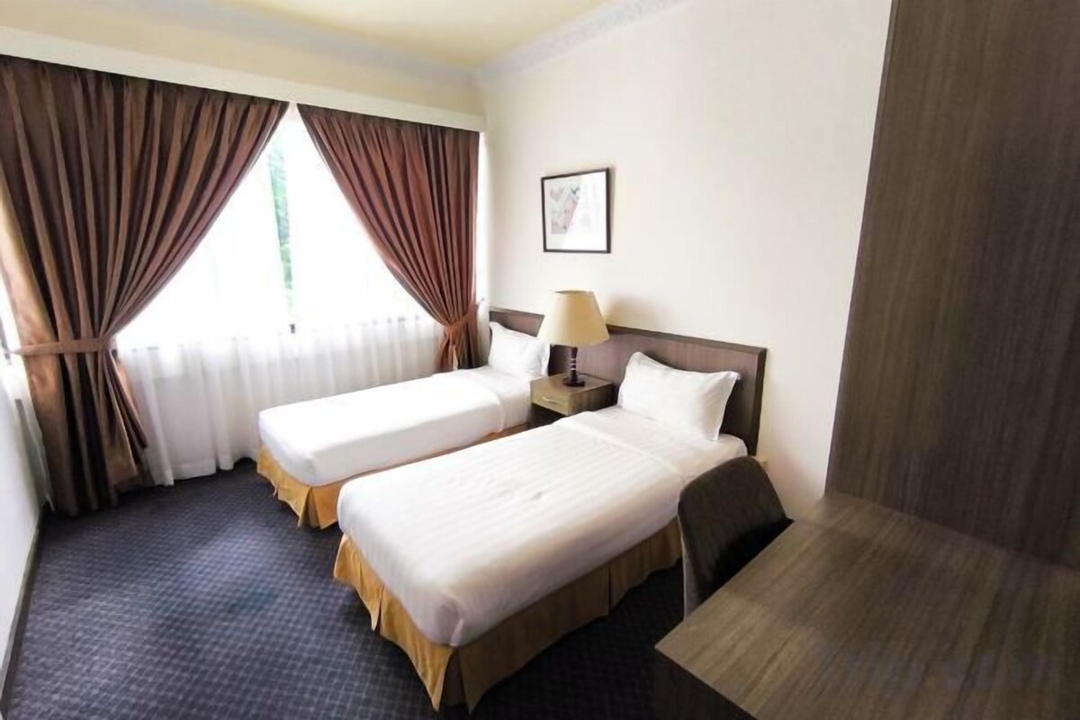 A hotel room with two beds, a nightstand, a lamp, and a window with curtains.