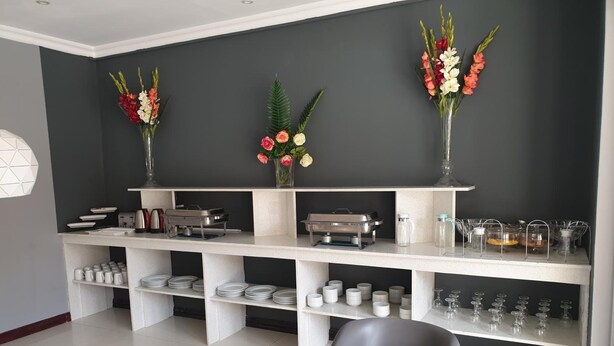 A modern kitchen with white cabinetry, a glass dining table, and a black chair. There are three vases with flowers on the wall, and various kitchen appliances and utensils on the countertops.