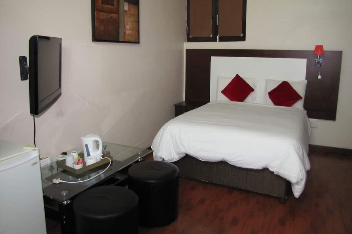 Habitación de hotel con cama, escritorio con cafetera, televisor y lámpara roja.