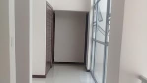 A corridor with tiled flooring, white walls, and large windows.