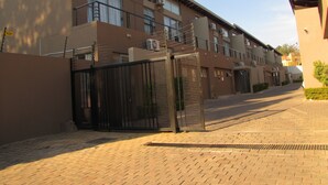 A multi-story building with a gated entrance, air conditioning units, and a paved driveway.