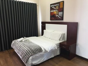 Une chambre d’hôtel avec un lit, une table de chevet, un tableau au mur et une fenêtre avec des stores.