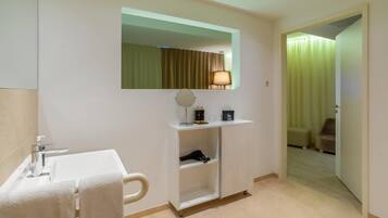 A hotel bathroom with a sink, mirror, towel rack, and a shelf with toiletries.