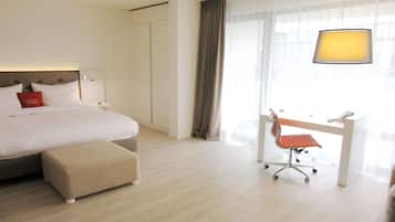 A hotel room with a bed, a desk with a chair, a lamp, and a window with curtains.