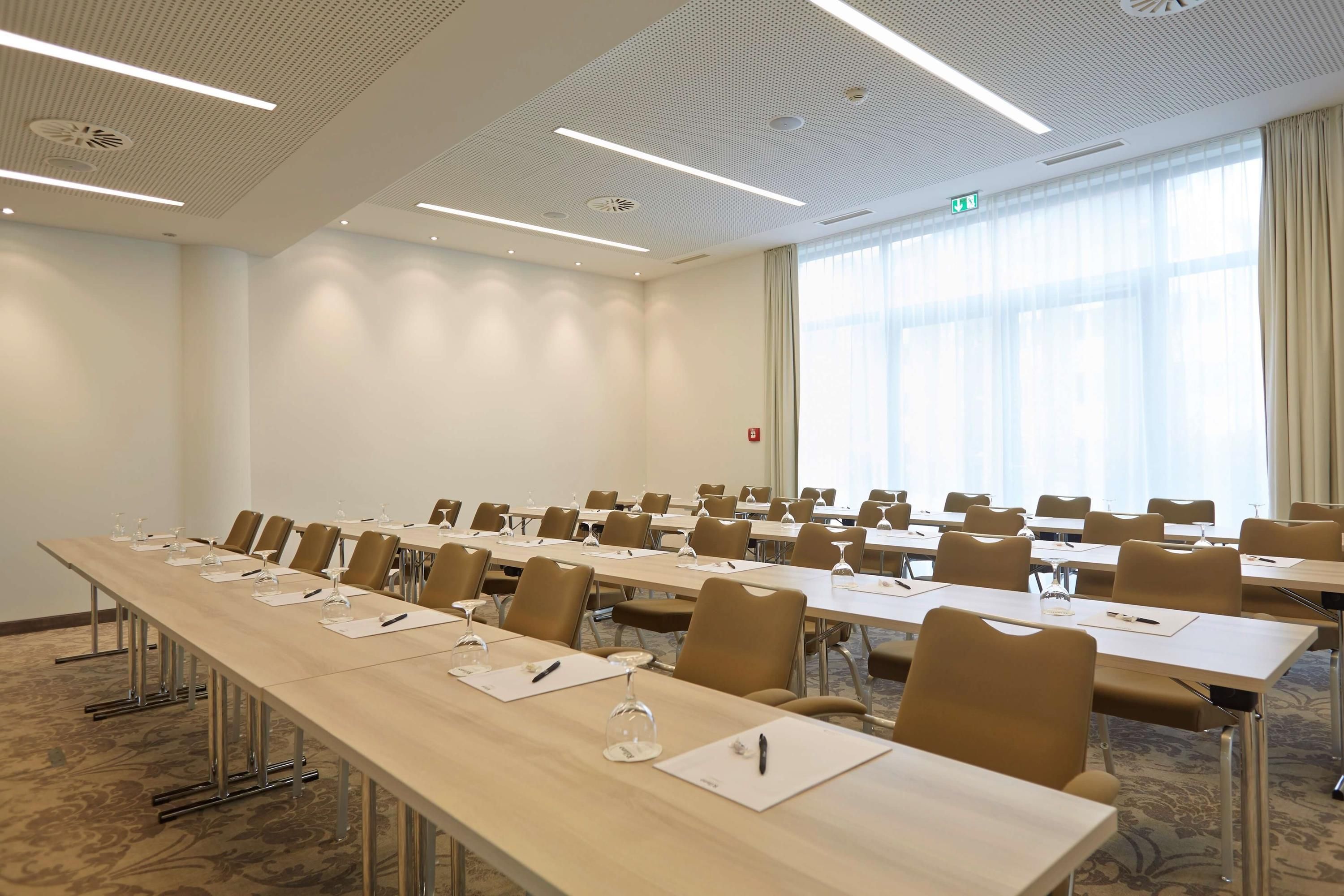 Un salón de conferencias con mesas largas, sillas y vasos.