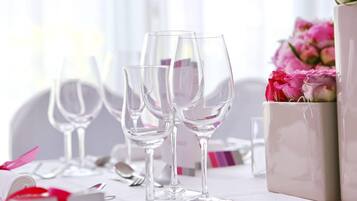 Una mesa dispuesta con copas de cristal, un jarrón con flores rosadas y una caja blanca.