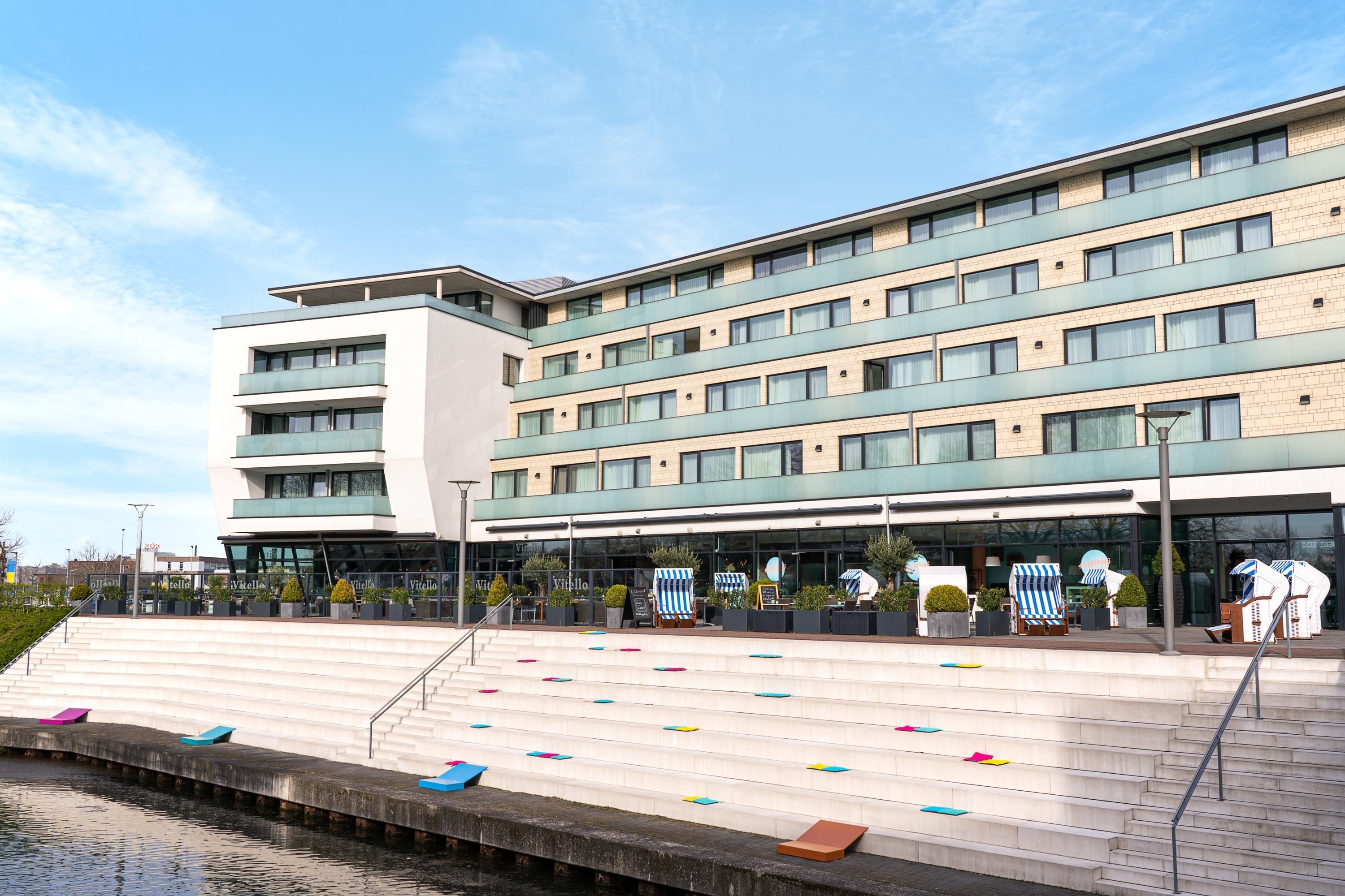 Un hôtel moderne à plusieurs étages, doté d’une terrasse et d’un élément décoratif aquatique.