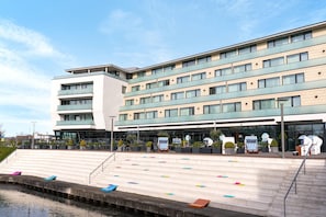 Ein modernes Hotel mit mehreren Etagen, Außenbereich und Blick auf das Wasser.