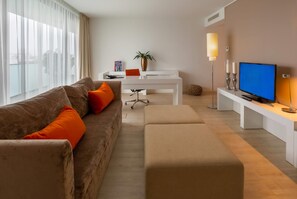 Una sala de estar moderna con un sofá marrón, cojines naranjas, una mesa de centro blanca, un televisor y una planta.