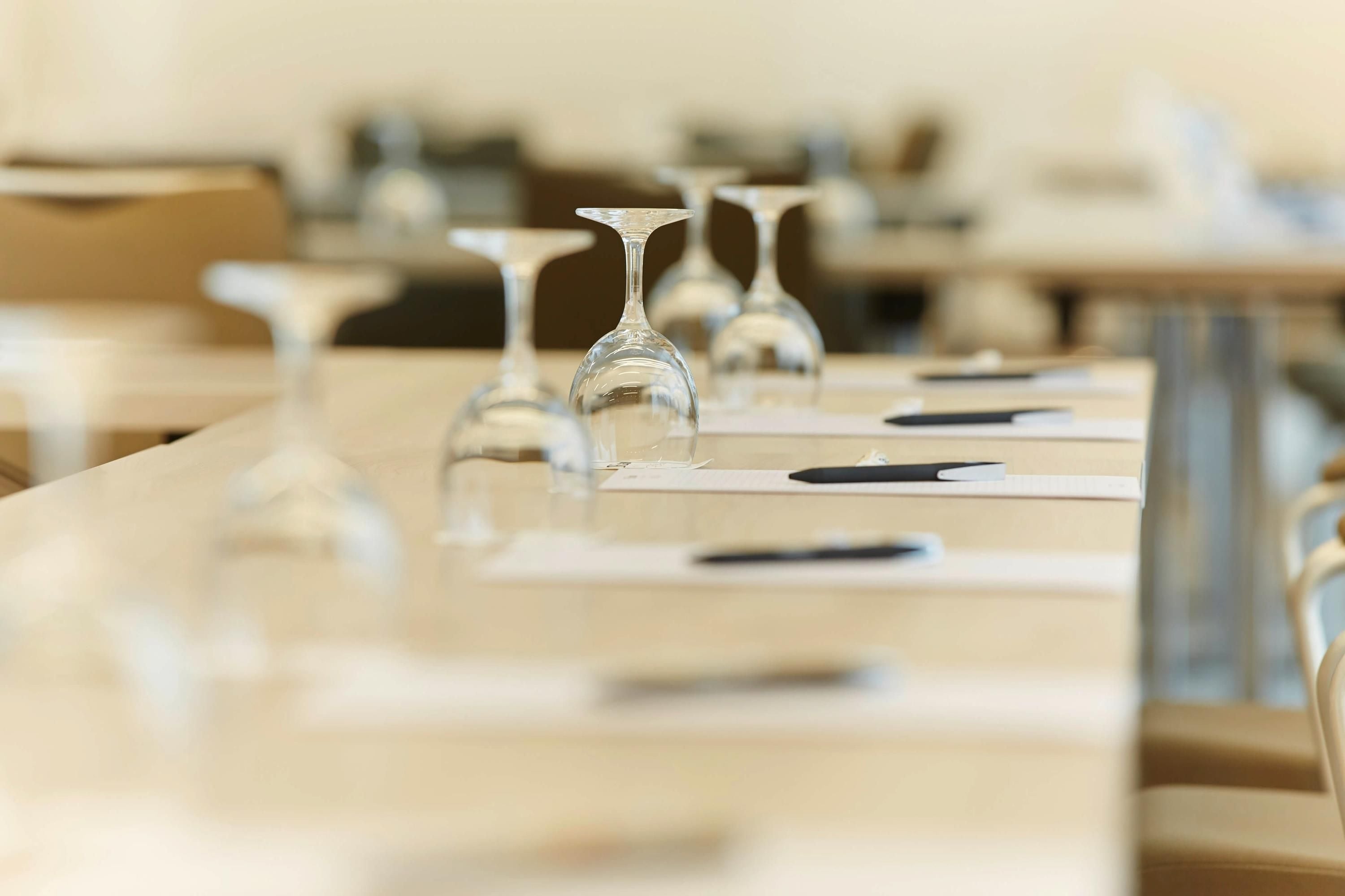 A classroom with rows of tables, each with a wine glass and a black pen on a notepad.