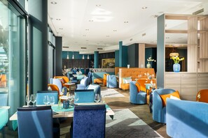 A modern restaurant with blue and orange seating, a bar area, and a visible menu board. - elaya hotel kleve, Trademark Collection by Wyndham (Kleve)