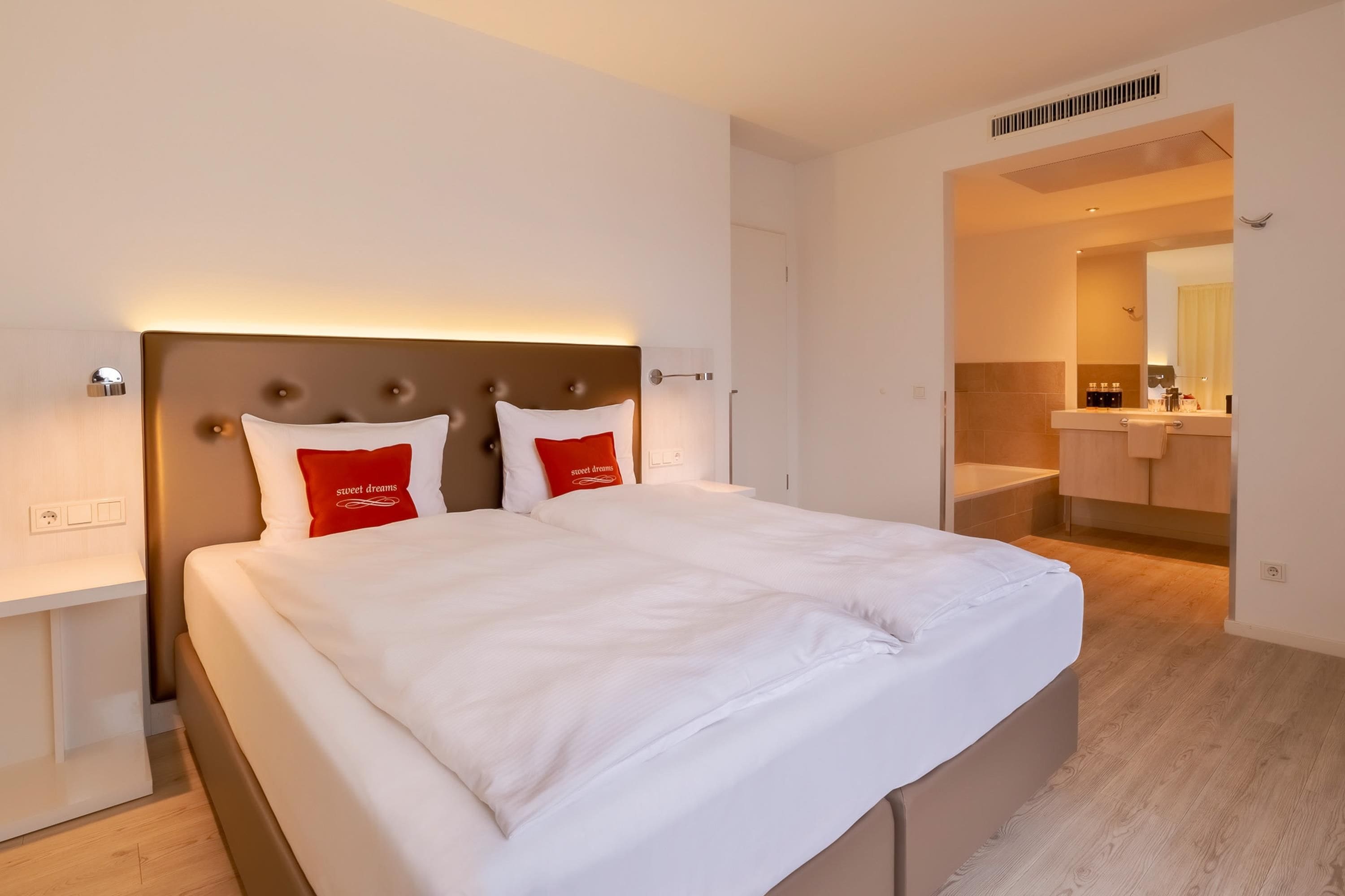A hotel room with a large bed, a nightstand, a bathroom with a bathtub, and a mirror.