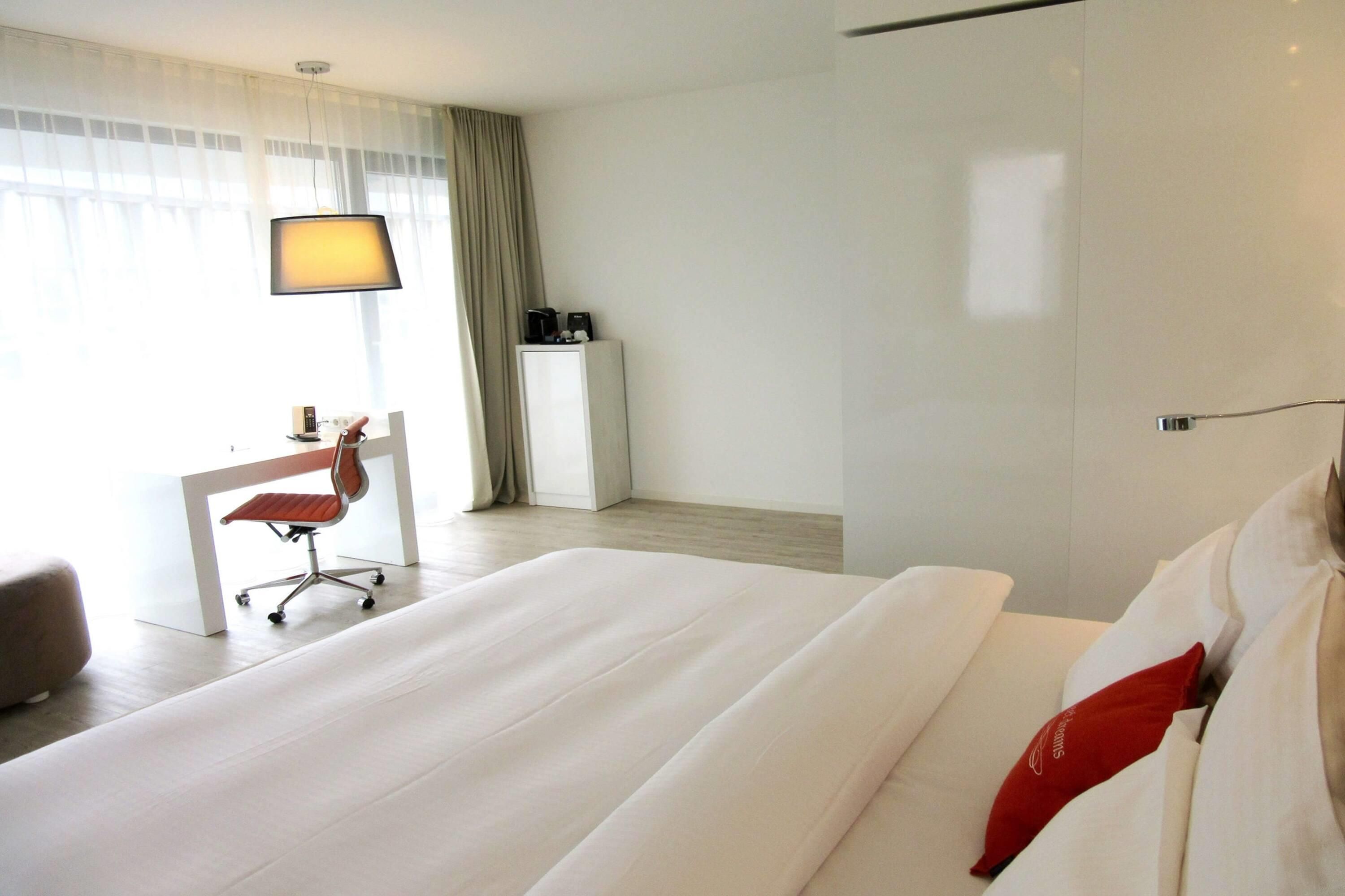 Ein Hotelzimmer mit einem großen Bett, einem Schreibtisch mit Stuhl, einer Lampe und einer Minibar.