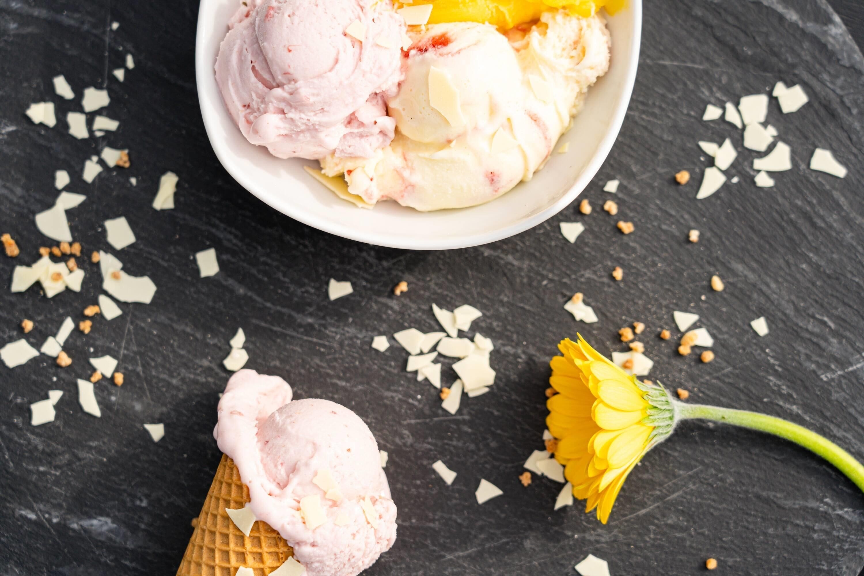 A bowl of ice cream with a waffle cone and a flower on a dark surface.