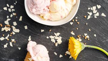 A bowl of ice cream with a waffle cone and a flower on a dark surface.
