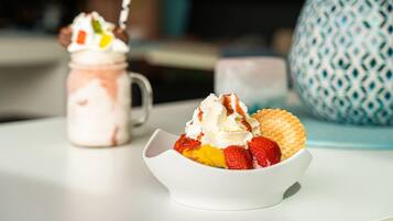 A dessert with whipped cream and strawberries in a white bowl, a jar with a similar dessert, and a patterned blue mug in the background.