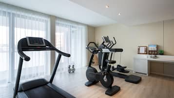 A modern home gym with a treadmill, elliptical, and stationary bike, large windows with sheer curtains, and a clean, minimalist design.