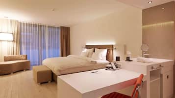 Ein Hotelzimmer mit Bett, Schreibtisch, Stuhl, Nachttisch, Lampe, Spiegel und einem Fenster mit Vorhängen.