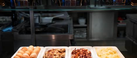 Un bufé con diversas opciones de comida, incluyendo huevos, salchichas y frijoles horneados.