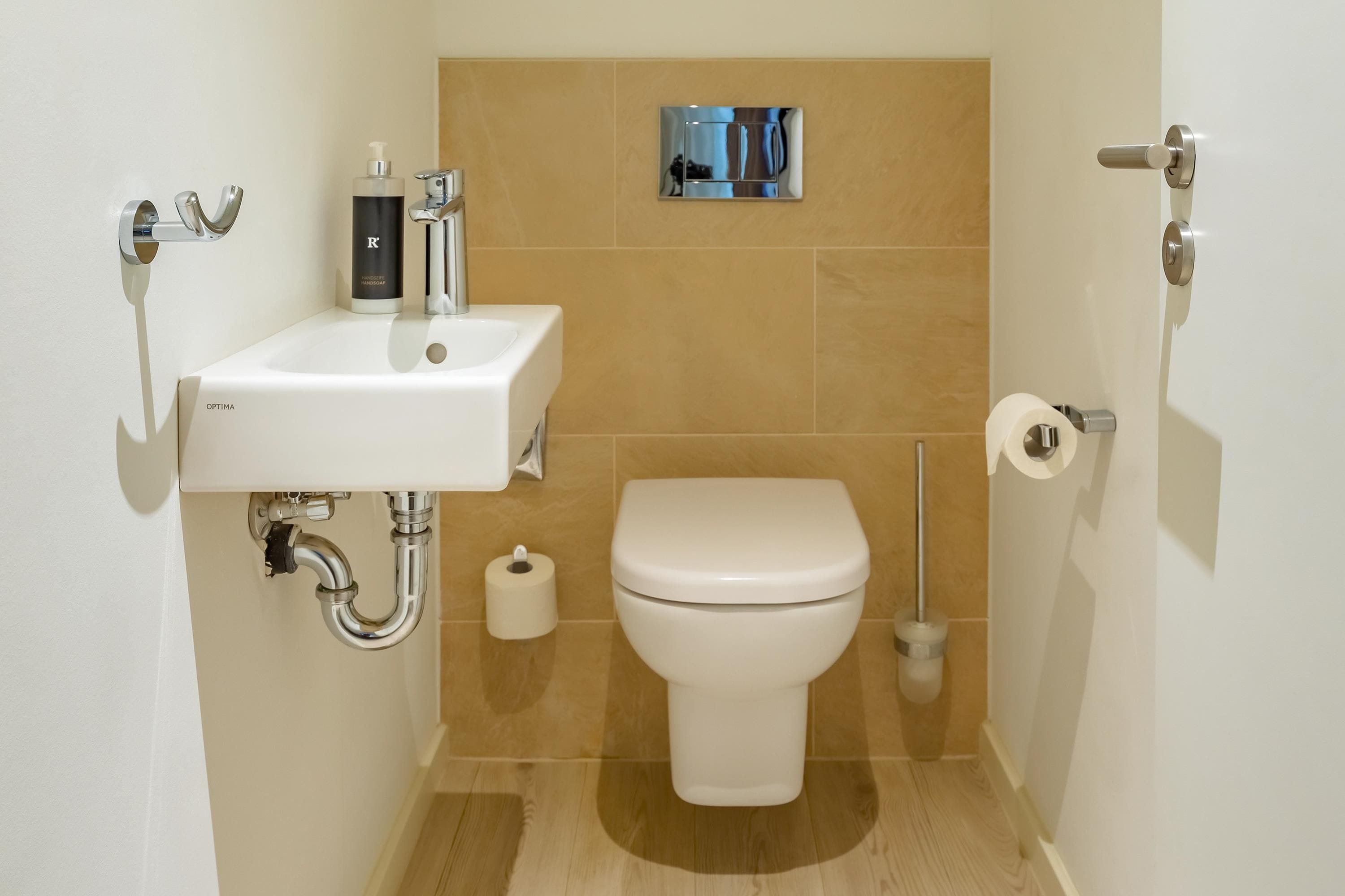 A compact bathroom with a white sink, a toilet, and a hand soap dispenser.