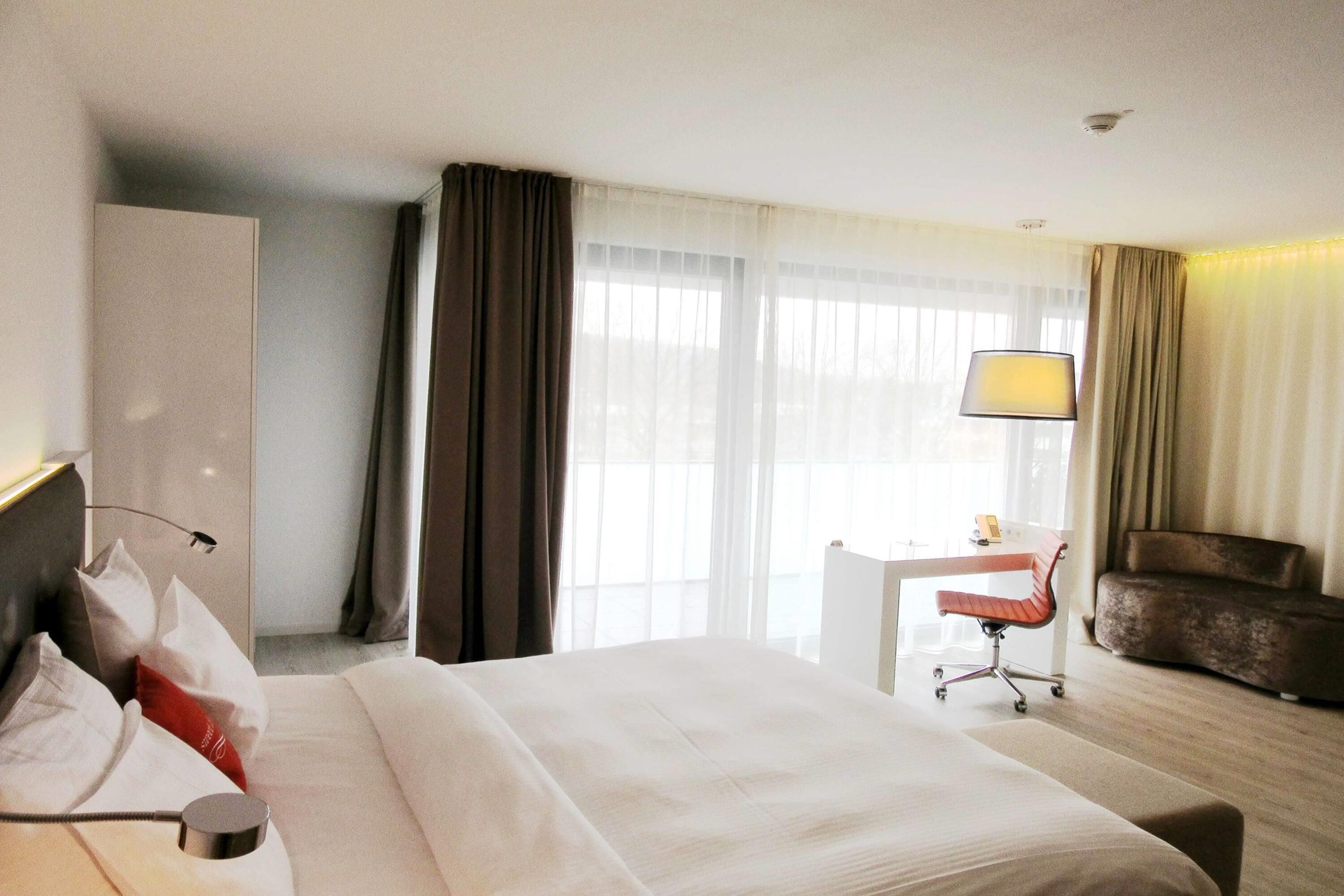 A hotel room with a bed, a desk, a chair, and a lamp.