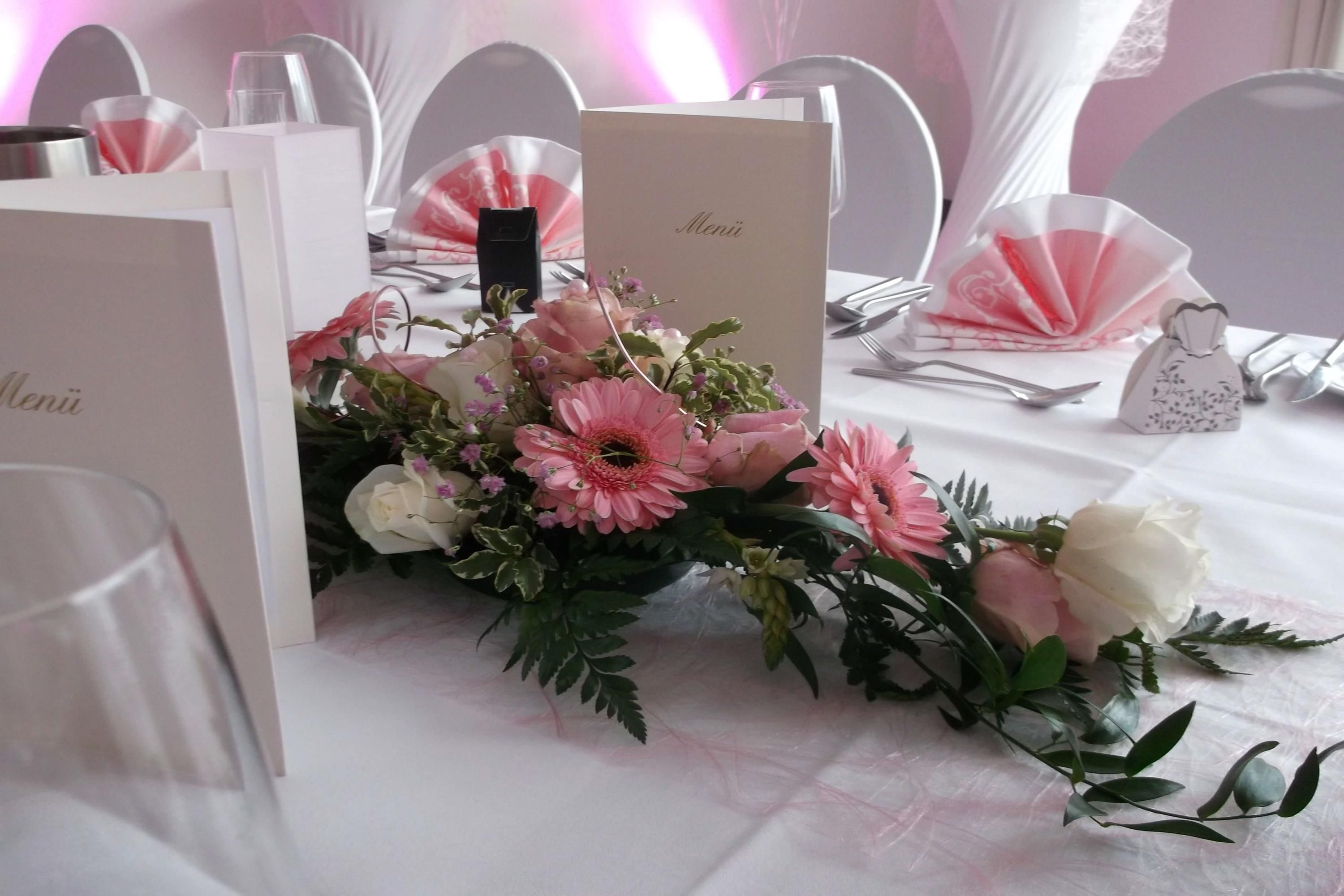 Une table dressée avec un menu, une composition florale et un verre d’eau.