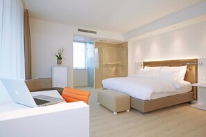 A modern hotel room with a bed, a desk with a laptop, a shower area, and a small seating area. - elaya hotel kleve, Trademark Collection by Wyndham (Kleve)