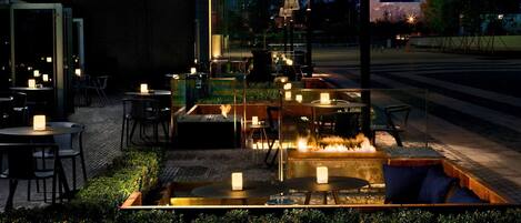 An outdoor seating area with tables and chairs, a fire feature, and a brick wall.