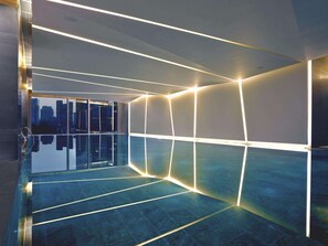 Una piscina interior moderna con iluminación geométrica y vistas a la ciudad.