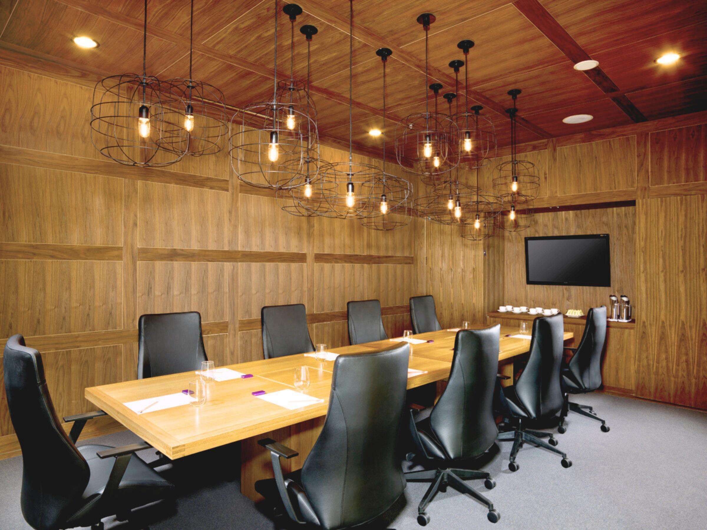 Un salón de conferencias con una larga mesa de madera, sillas negras y lámparas colgantes.