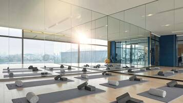 Ein geräumiger Yogaraum mit mehreren Matten und Blöcken, großen Fenstern mit Blick auf die Stadt und einem modernen Interieur.